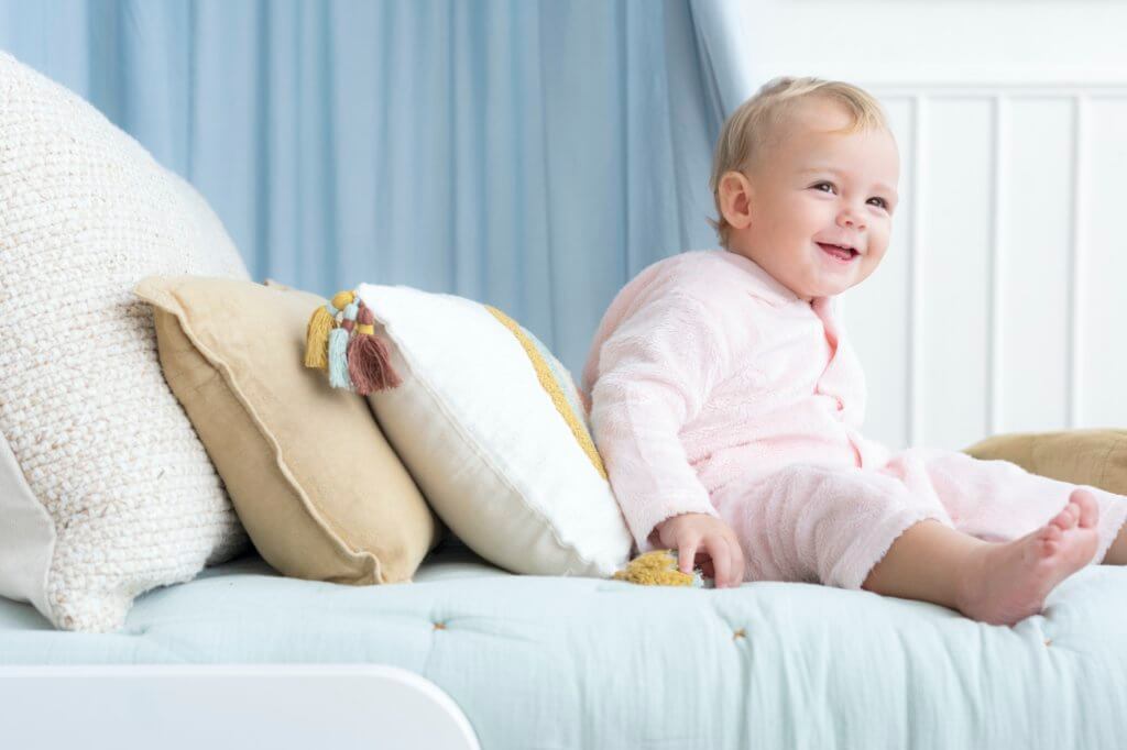 Happy baby sitting on a bed and smiling