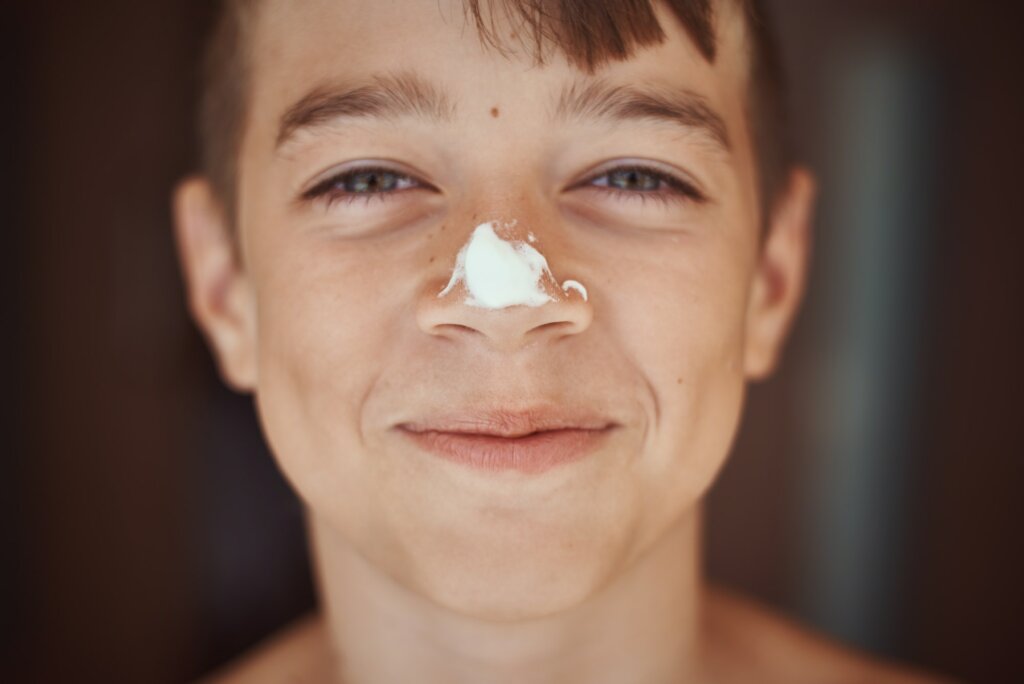 Happy smile boy with sunscreen cream on the nose, close up portrait